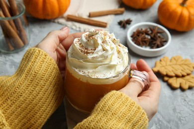 Photo of Woman holding cup of pumpkin spice latte with whipped cream at light grey table, closeup