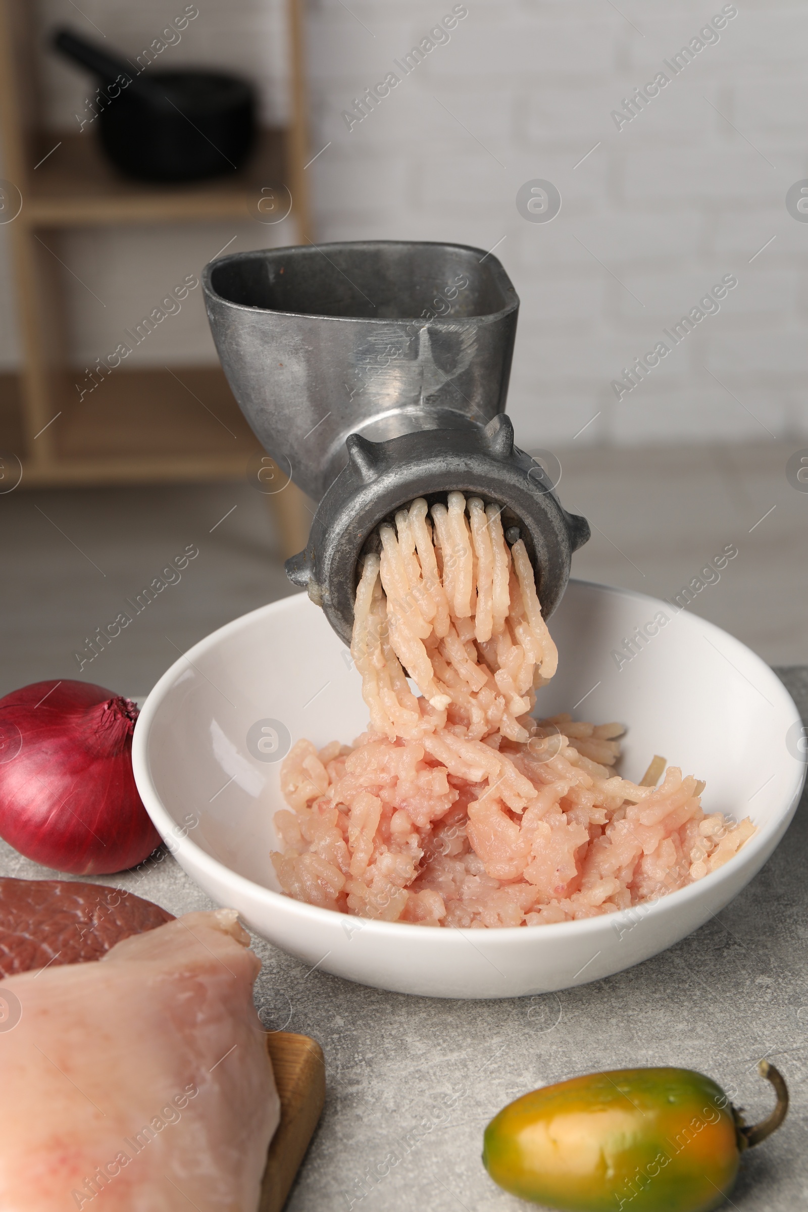 Photo of Metal meat grinder with chicken mince and products on light grey table indoors
