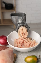 Metal meat grinder with chicken mince and products on light grey table indoors