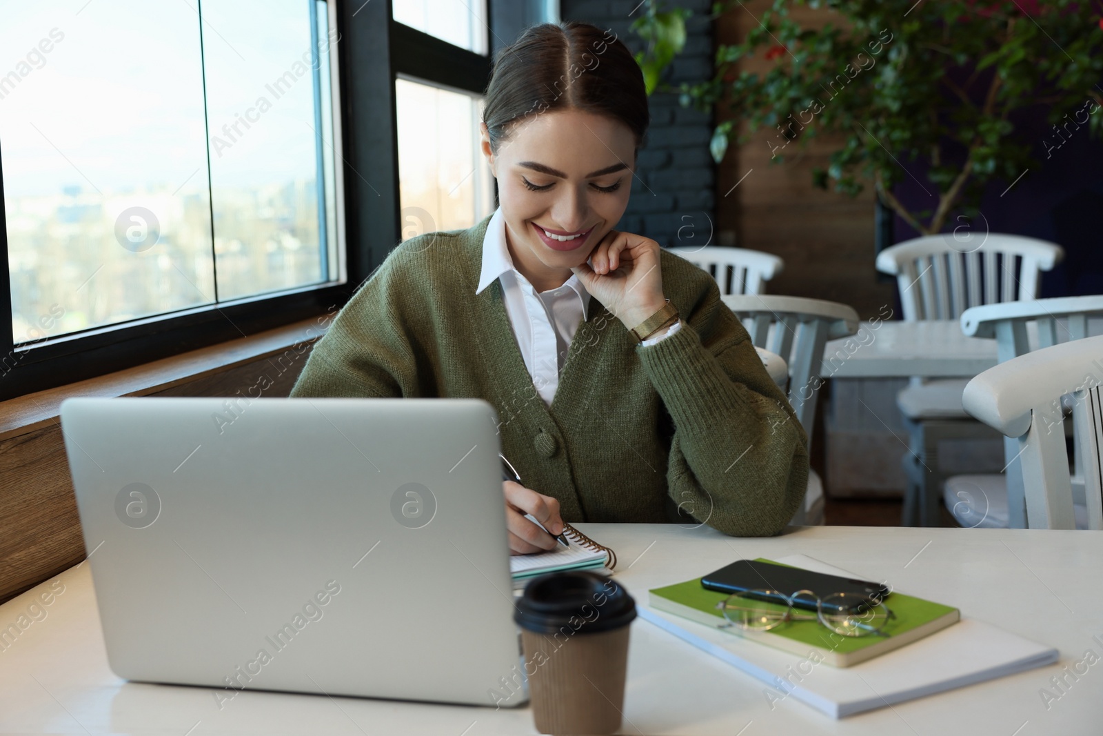 Photo of Young female student with laptop studying at table in cafe