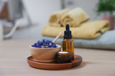 Photo of Bottle of essential oil, dry flowers and jar with cream on light wooden table. Spa therapy