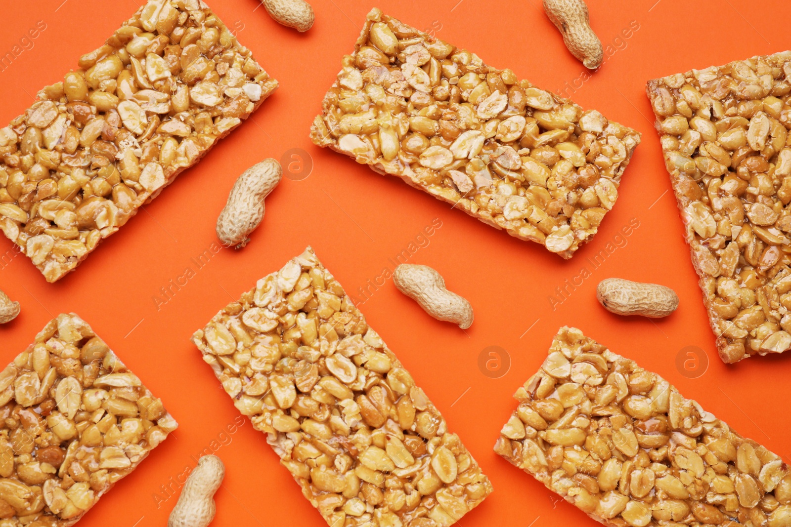 Photo of Tasty kozinaki bars and peanuts on orange background, flat lay
