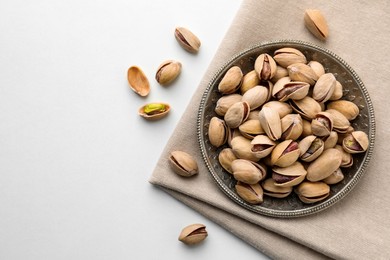 Photo of Plate and pistachio nuts on white background, flat lay. Space for text