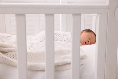 Photo of Cute newborn baby sleeping under plaid in crib