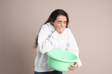 Young woman with basin suffering from nausea on beige background. Food poisoning