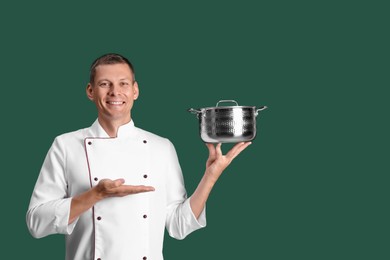 Photo of Happy male chef with cooking pot on dark green background. Space for text