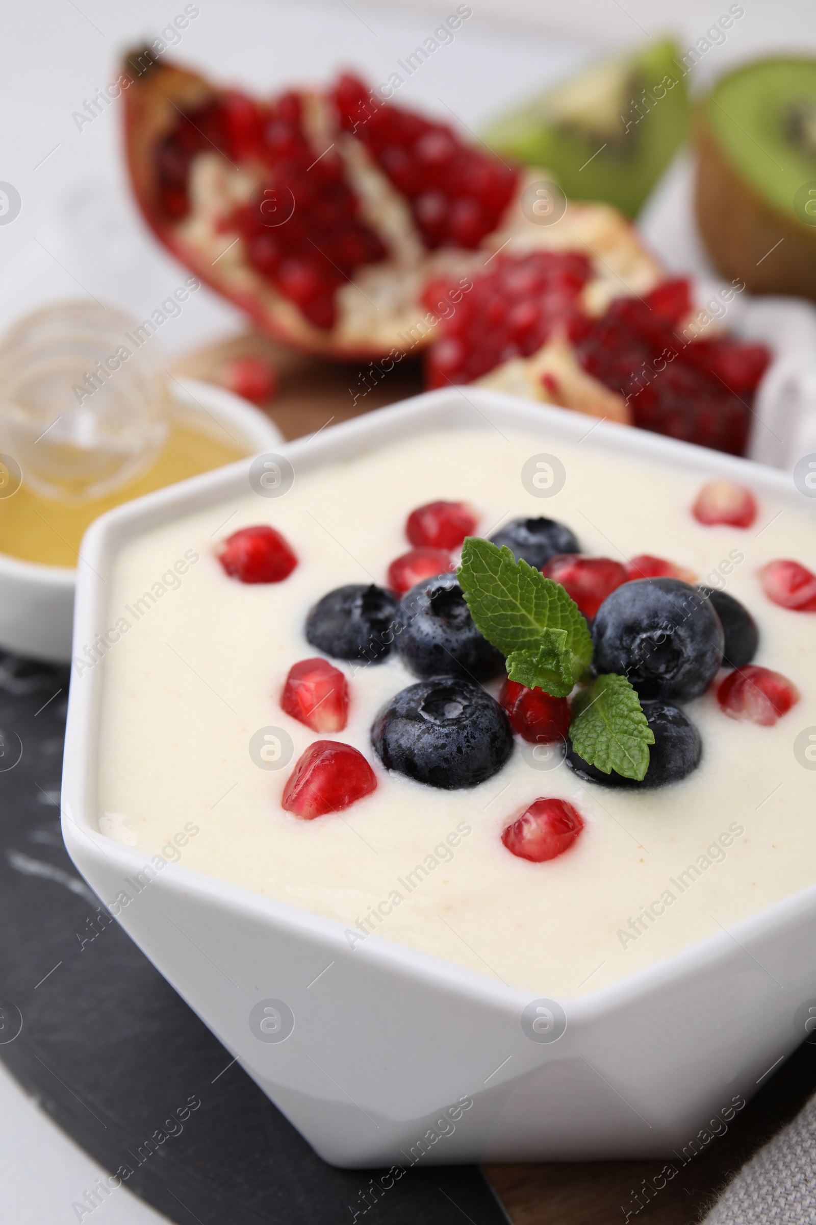 Photo of Bowl of delicious semolina pudding with blueberries, pomegranate and mint on table, closeup