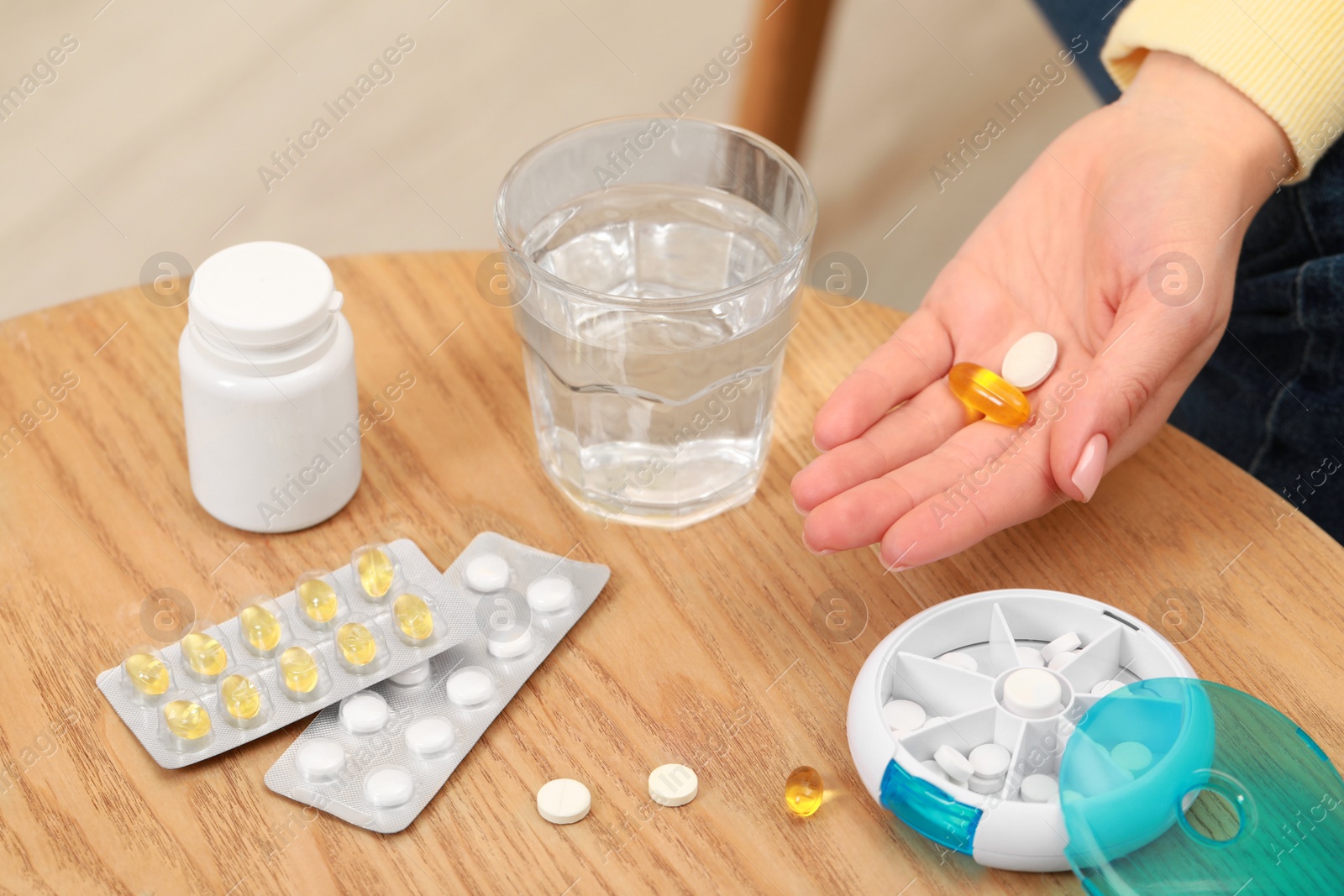 Photo of Woman holding pills at table with plastic box and different medicaments indoors, closeup