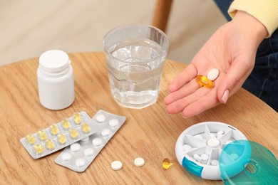 Photo of Woman holding pills at table with plastic box and different medicaments indoors, closeup