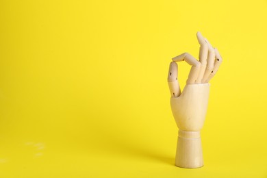Wooden mannequin hand showing okay gesture on yellow background. Space for text