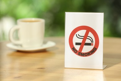Photo of No Smoking sign and cup of drink on wooden table outdoors. Space for text