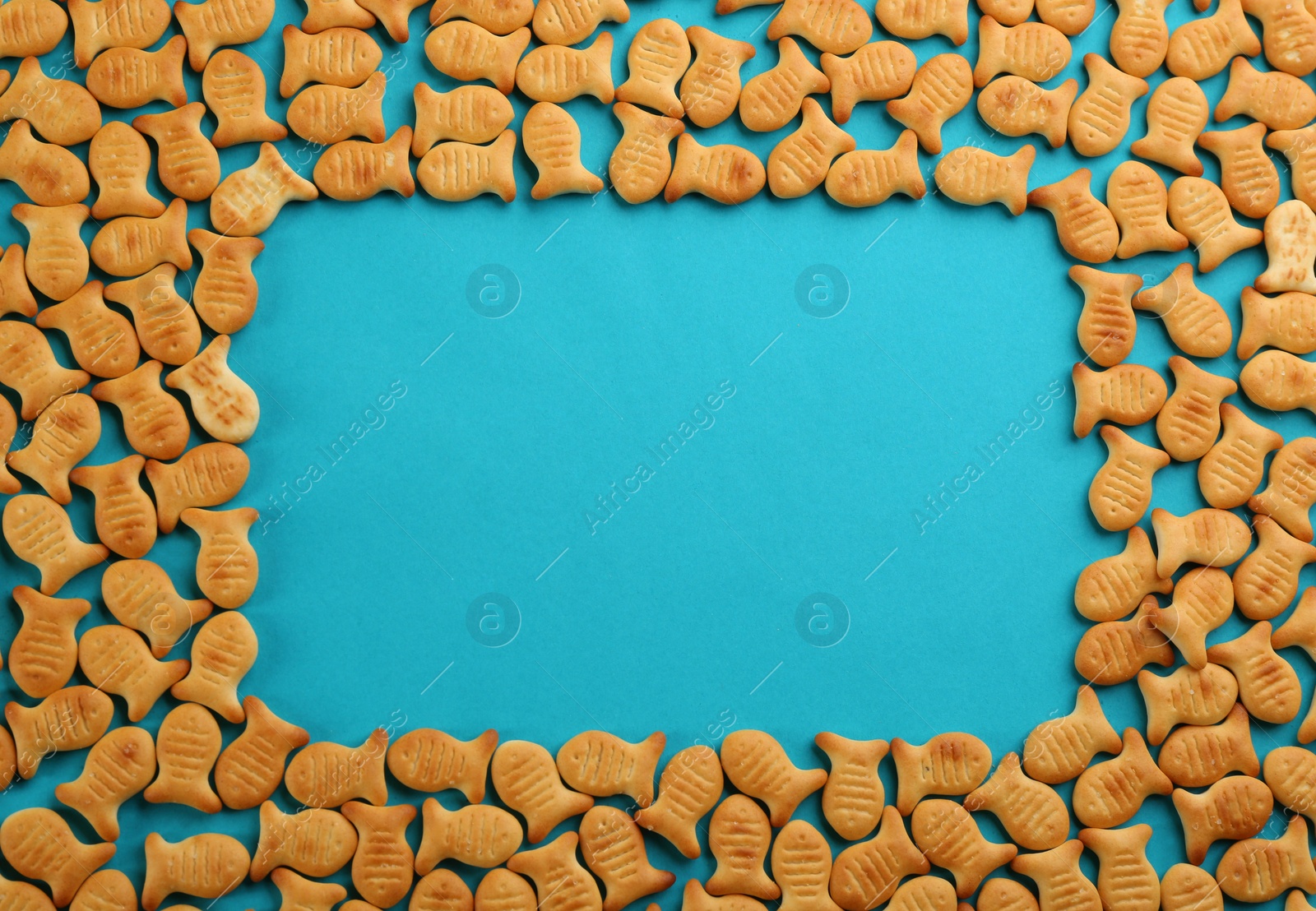 Photo of Frame of delicious goldfish crackers on blue background, flat lay. Space for text