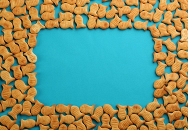 Frame of delicious goldfish crackers on blue background, flat lay. Space for text