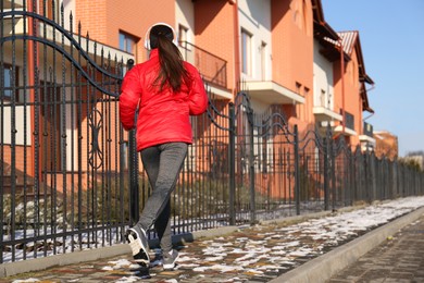 Photo of Woman running along street on winter day, back view. Outdoors sports exercises