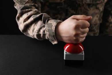 Serviceman pressing red button of nuclear weapon at black table, closeup. War concept