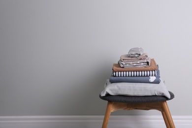 Stack of clean bed linen and pillow on stool near light grey wall. Space for text