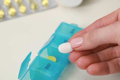 Photo of Woman taking pill from plastic container at white table, closeup