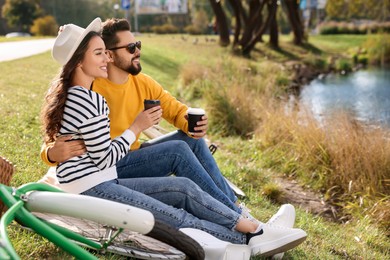 Beautiful young couple with takeaway coffee spending time together near pond in park