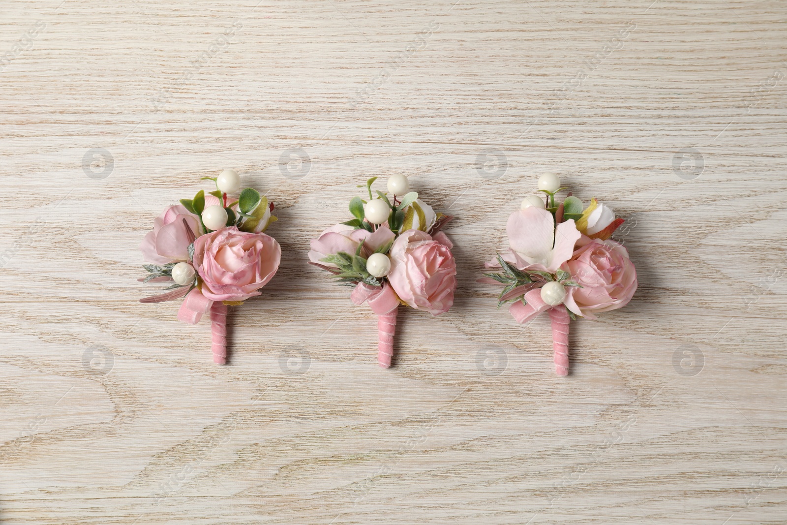 Photo of Stylish pink boutonnieres on white wooden table, flat lay