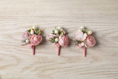 Stylish pink boutonnieres on white wooden table, flat lay