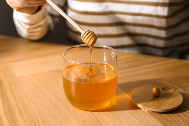 Photo of Woman with honey and dipper at wooden table, closeup