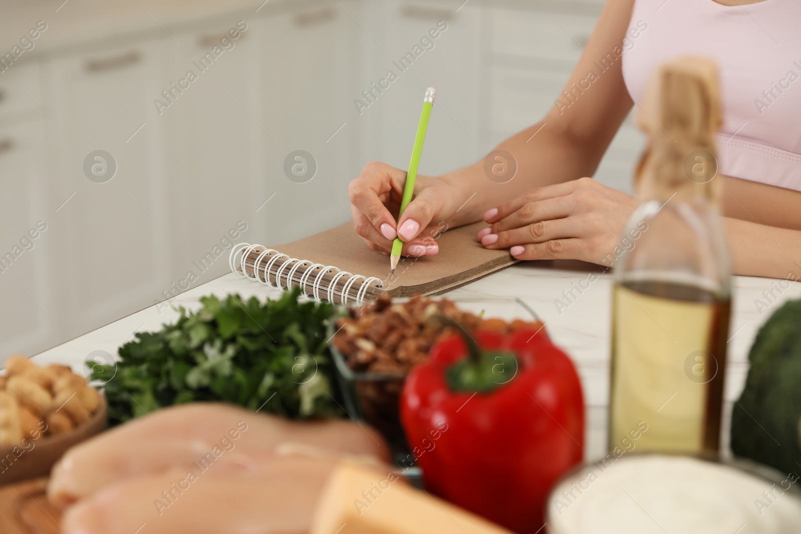 Photo of Woman writing in notebook near products at table, closeup. Keto diet