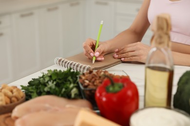 Woman writing in notebook near products at table, closeup. Keto diet