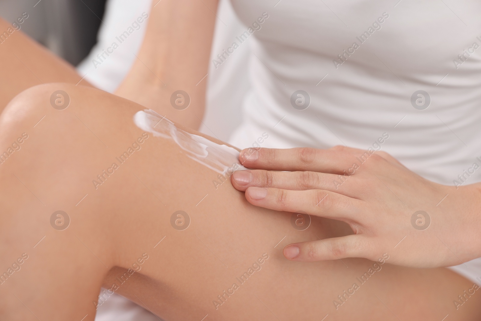 Photo of Woman applying cream onto leg in bed, closeup