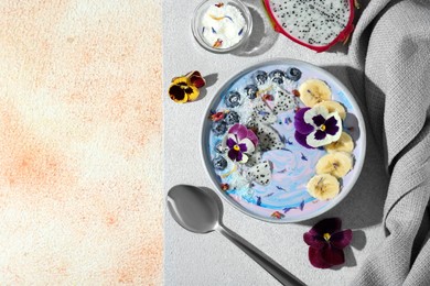 Delicious smoothie bowl with fresh fruits, blueberries and flowers served on color textured table, flat lay. Space for text