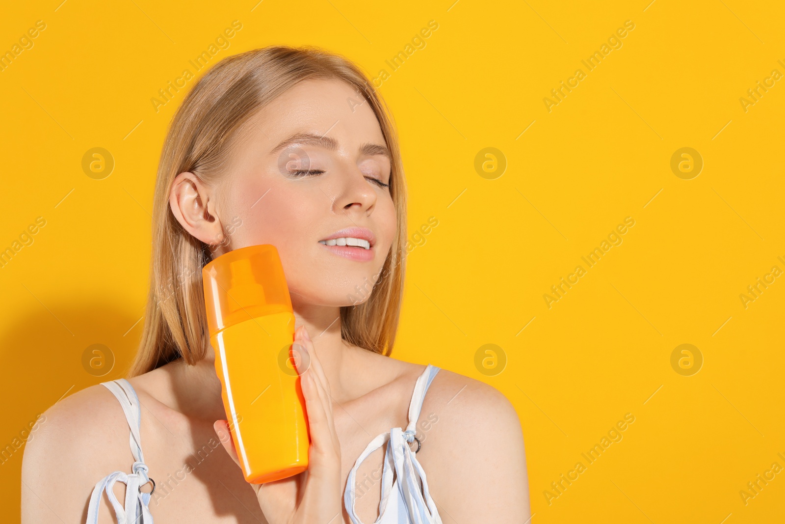 Photo of Beautiful young woman holding sun protection cream on orange background, space for text