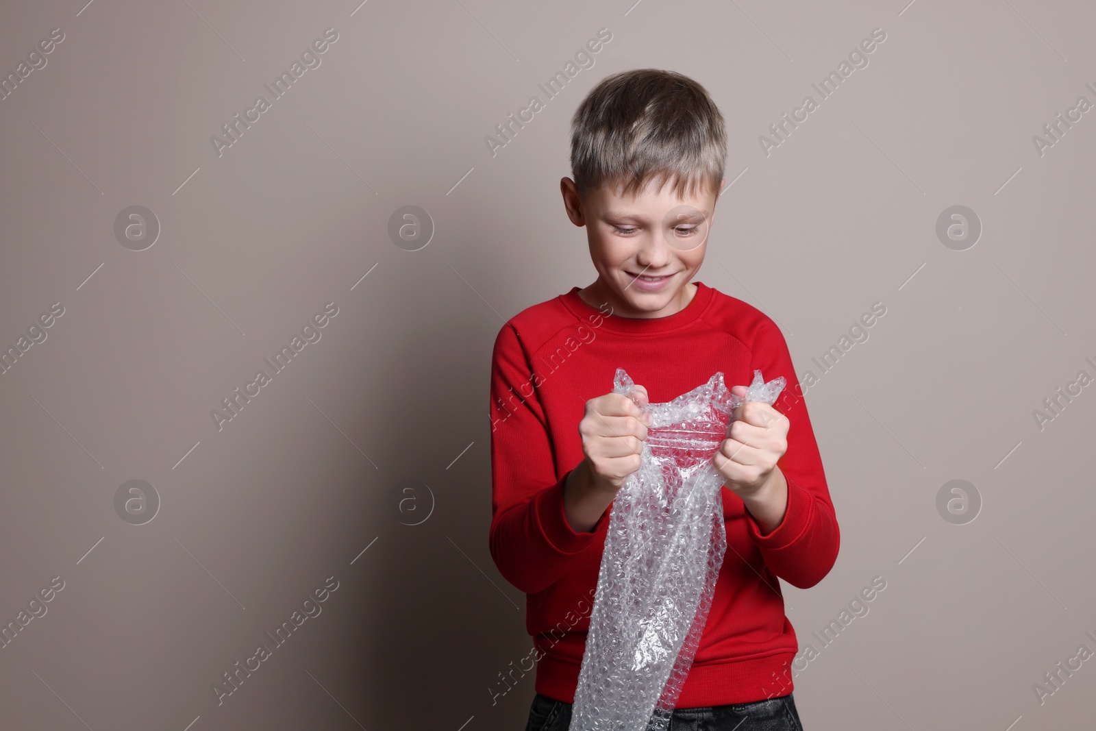 Photo of Happy boy popping bubble wrap on beige background, space for text. Stress relief