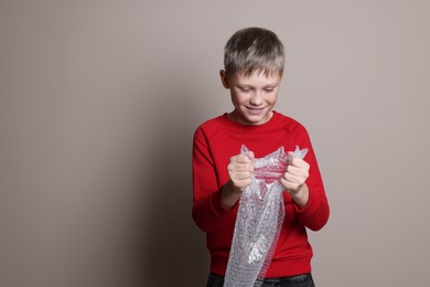 Happy boy popping bubble wrap on beige background, space for text. Stress relief