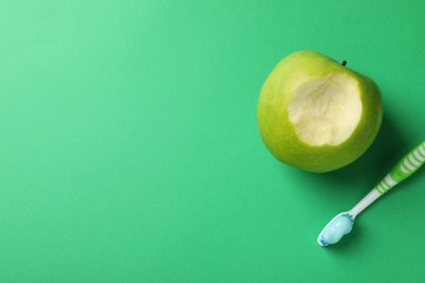 Photo of Toothbrush with paste and bitten apple on green background, flat lay. Space for text