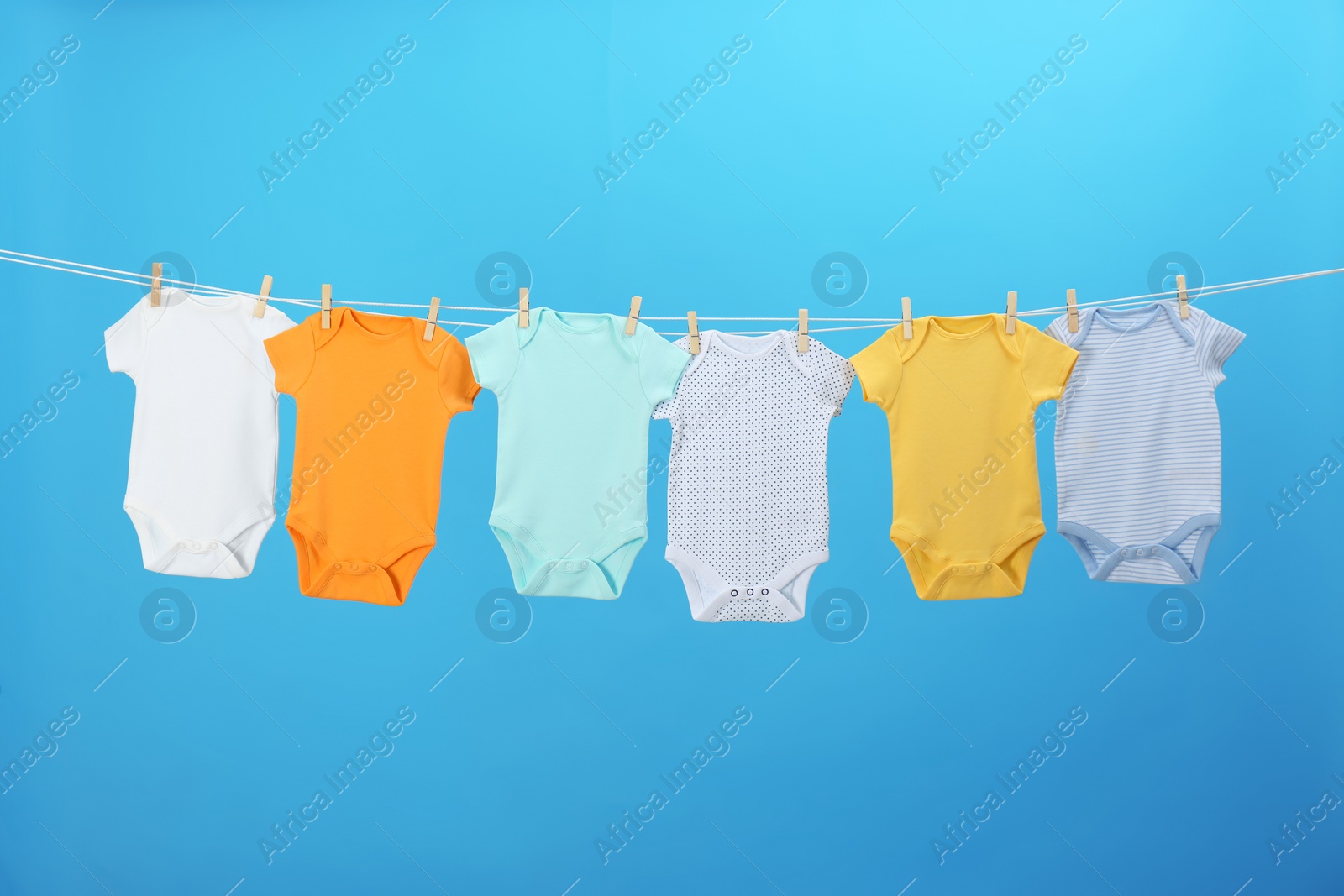 Photo of Colorful baby onesies hanging on clothes line against blue background. Laundry day