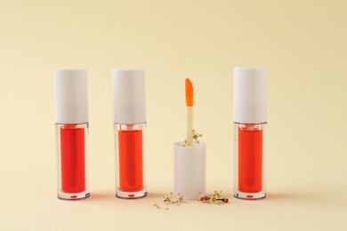 Photo of Bright lip glosses and applicator on beige background