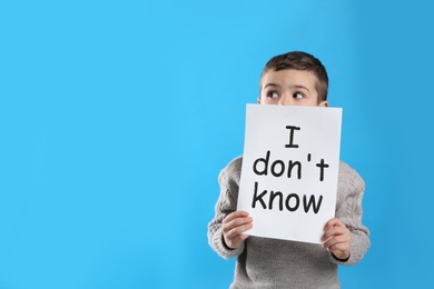 Emotional little boy holding paper with text I Don't Know on light blue background