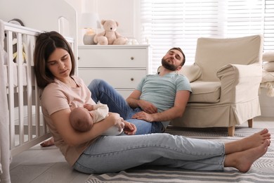 Photo of Tired young parents with their baby sleeping on floor in children's room