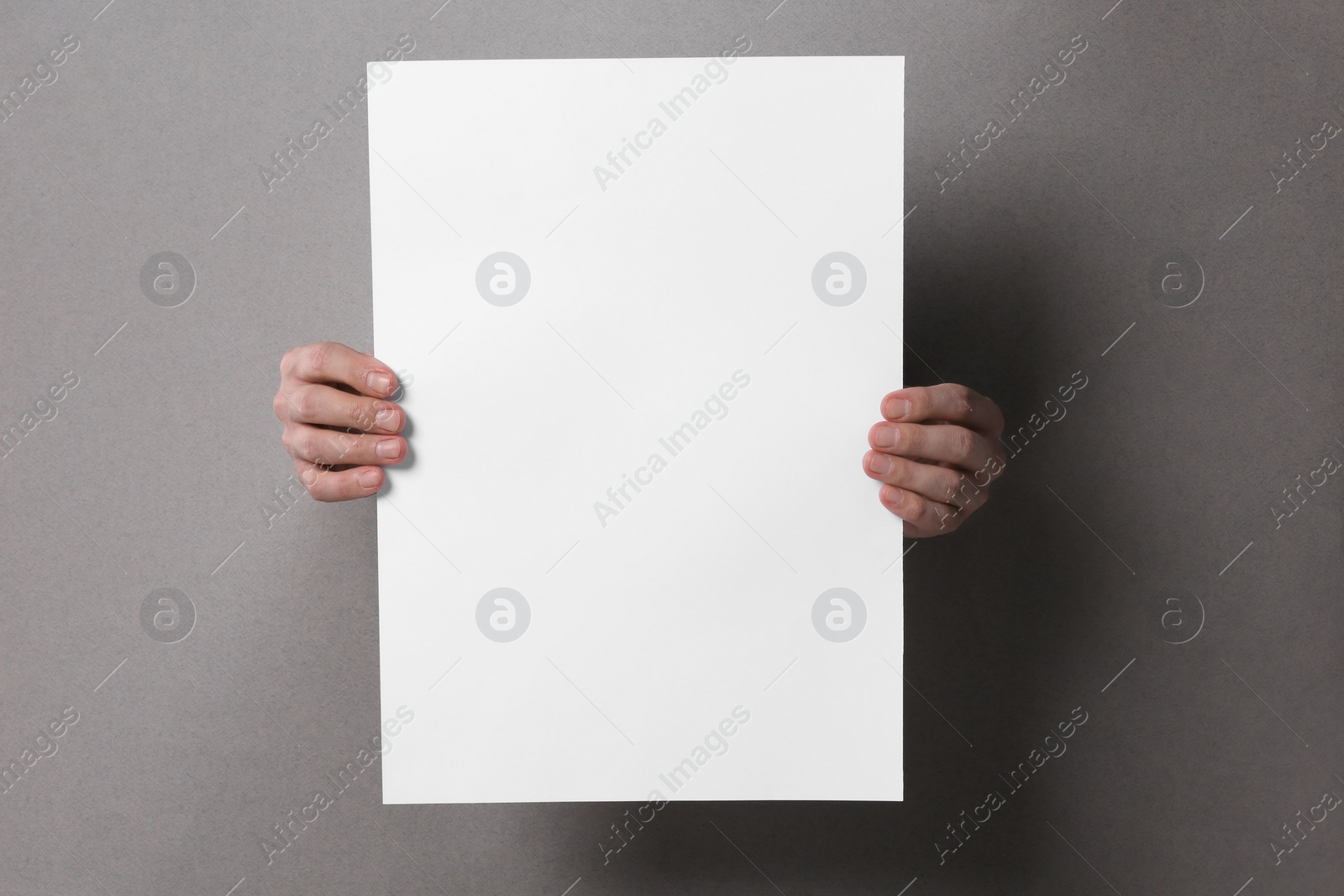 Photo of Man holding sheet of paper through holes in grey paper, closeup. Mockup for design