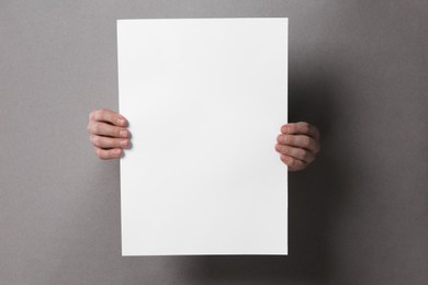 Man holding sheet of paper through holes in grey paper, closeup. Mockup for design