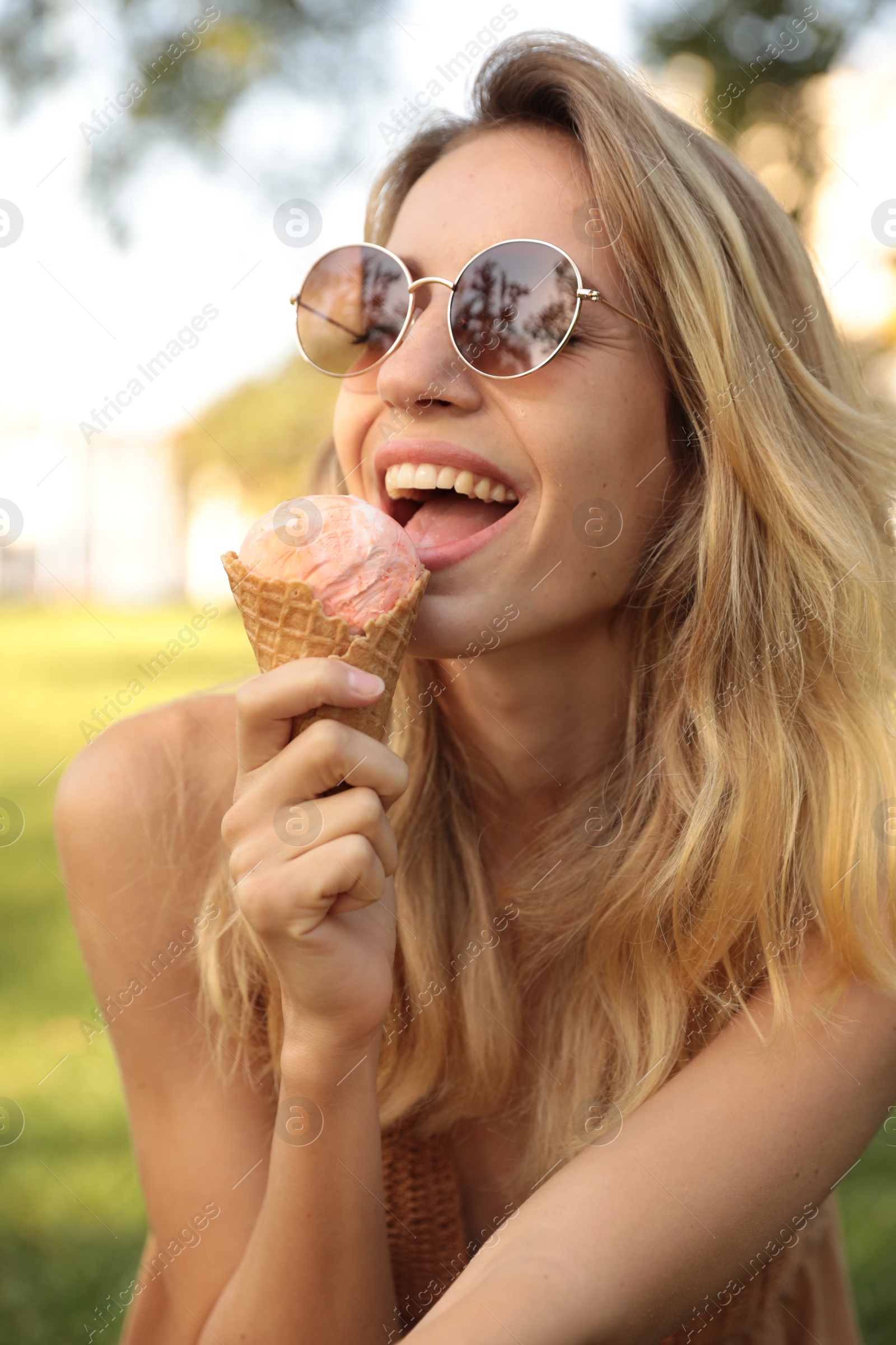 Photo of Happy young woman with delicious ice cream in waffle cone outdoors