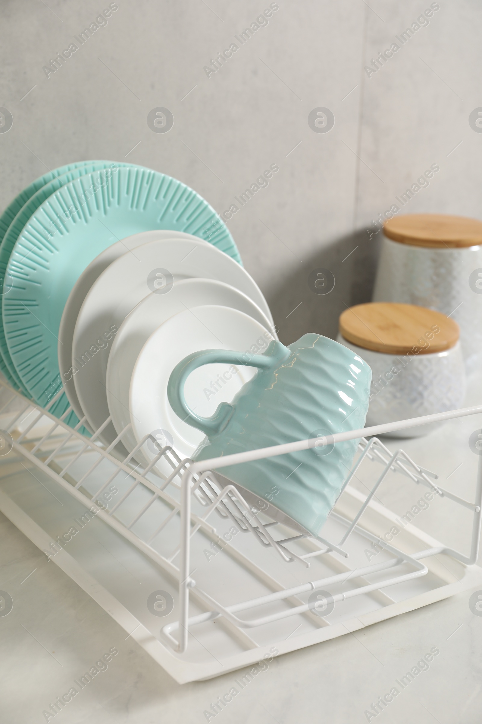 Photo of Drainer with different clean dishware and cup on light table indoors