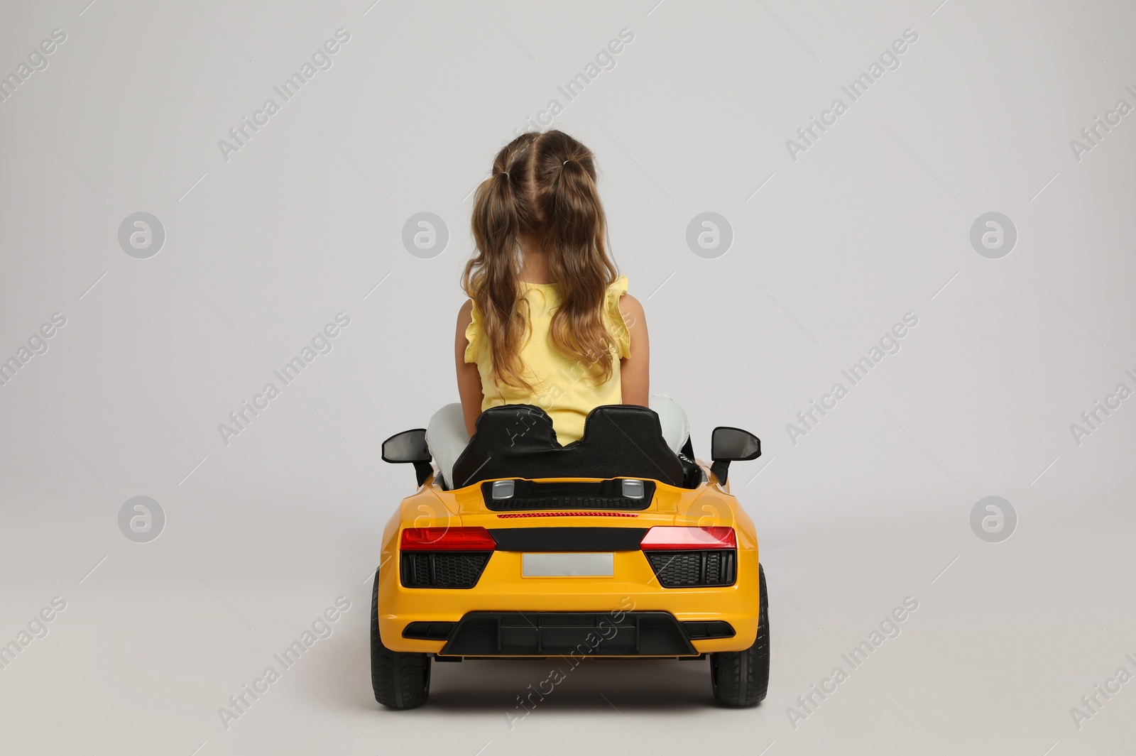 Photo of Cute little girl driving children's electric toy car on grey background, back view