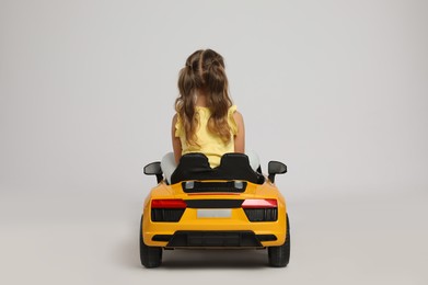 Cute little girl driving children's electric toy car on grey background, back view