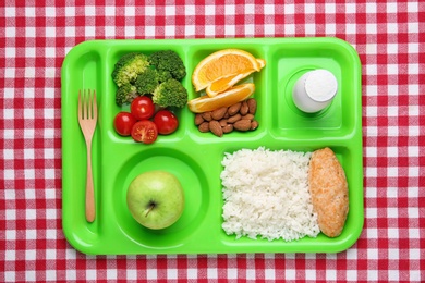 Photo of Serving tray with healthy food on checkered background, top view. School lunch