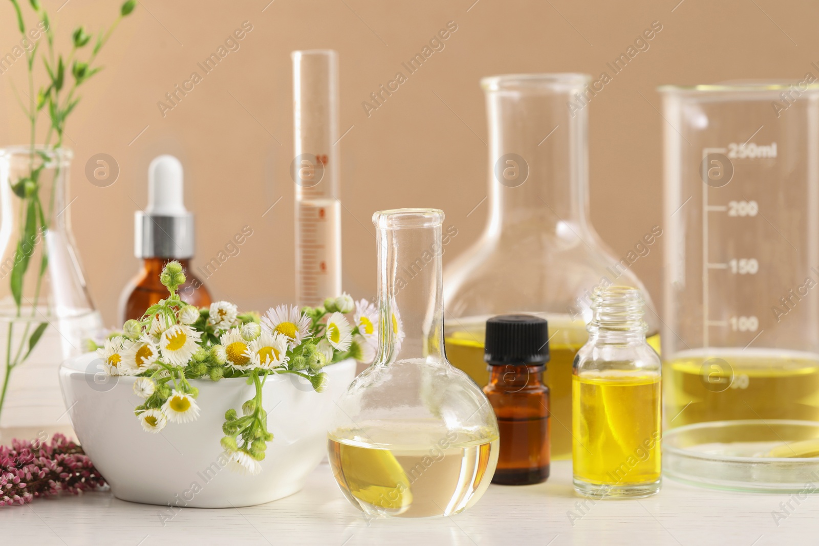 Photo of Developing cosmetic oil. Laboratory glassware and flowers on white wooden table