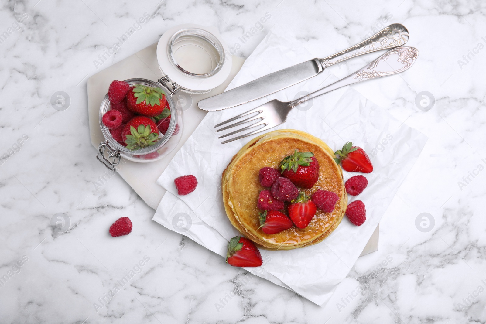 Photo of Tasty pancakes served with honey and berries on white marble table, flat lay