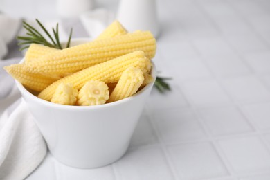 Photo of Tasty fresh yellow baby corns in bowl on white tiled table, closeup. Space for text