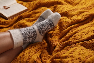Photo of Woman in warm socks resting on knitted blanket, closeup
