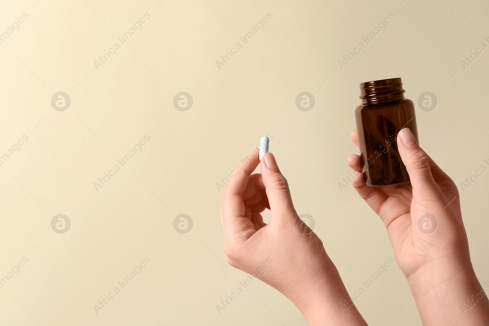 Photo of Woman holding pill and bottle on beige background, closeup. Space for text