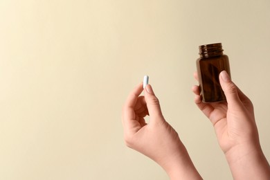 Woman holding pill and bottle on beige background, closeup. Space for text